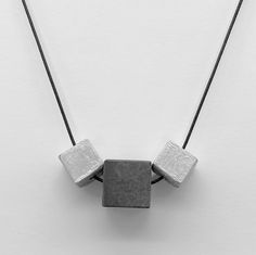 Discover the epitome of urban sophistication with our Adjustable Dual-Tone Concrete Necklace, showcasing handcrafted pendants in a sleek, geometric design. This statement piece features a trio of concrete cubes: two 12 mm cubes adorned with reflective silver acrylic paint and a central 16 mm cube in a chic dark grey. All suspended on a versatile cord adjustable up to 70 cm, this necklace is the perfect fusion of industrial charm and modern elegance. Elevated Urban Aesthetic: Silver accents bring Concrete Necklace, Contemporary Jewelry Design, Urban Sophistication, Urban Aesthetic, Geometric Pendant, Contemporary Jewelry, Silver Accents, Unique Necklaces, Modern Elegance