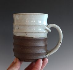 a hand holding a white and brown coffee mug