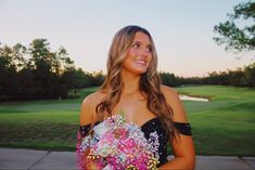 a beautiful woman holding a bouquet of flowers in front of a golf course at sunset