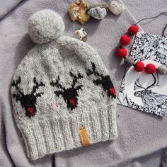 a knitted hat with reindeers and pom - poms sits on top of a blanket