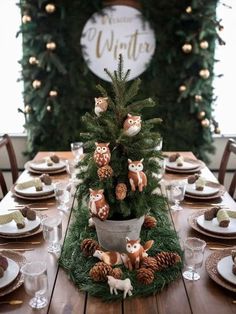 a christmas table setting with pine cones and fake animals on the centerpiece, surrounded by greenery