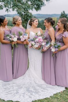 a group of women standing next to each other in front of a tree holding bouquets