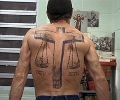 a man with his back turned to the camera, has a tattoo on his chest that says truth and justice