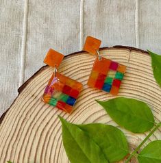 Add a pop of color to your outfit with these Handmade Colorful Orange Resin Square Earrings. These unique earrings feature a vibrant multicolored resin that will make a statement wherever you go. The dangle design adds a touch of fun and movement to your look, while the lightweight materials ensure all-day comfort. Handcrafted with care, these earrings are perfect for women who want to stand out and express their individual style. Whether you're dressing up for a special occasion or adding a tou Handmade Multicolor Square Earrings, Square Multicolor Earrings For Gift, Vibrant Multicolor Dangle Earrings, Handmade Retro Multicolor Earrings, Multicolor Rectangular Earrings As A Gift, Multicolor Rectangular Earrings For Gifts, Resin Square, Orange Resin, Square Earrings