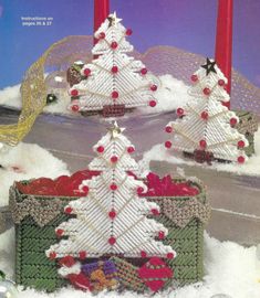 two knitted christmas trees sitting on top of snow covered ground next to red candles