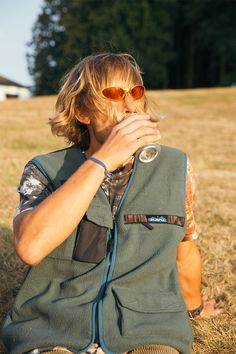 a man sitting on the ground drinking from a cup with his hands in his mouth