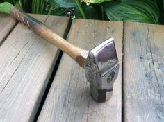 an old hammer is sitting on top of a wooden table next to green plants and flowers