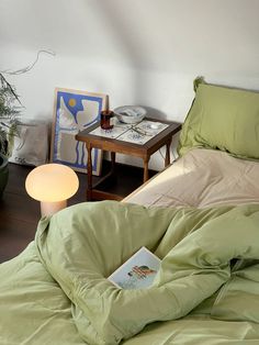 an unmade bed in a bedroom with green sheets and pillows on the floor next to a lamp