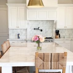 a white kitchen with marble counter tops and chairs in front of an island that has flowers on it