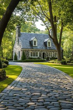 a cobblestone road leading to a stone house with trees in the foreground