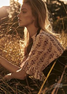 a woman sitting in tall grass with her hand on her hip and looking off into the distance