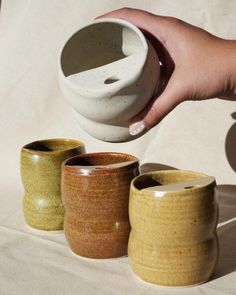 a person is pouring something into three different cups on a white tablecloth, with one hand reaching for the cup