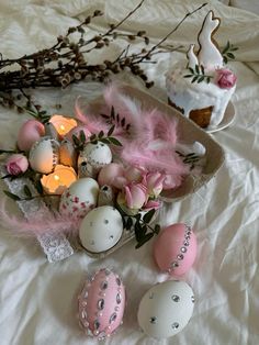 some pink and white decorated eggs on a bed with flowers, candles and branches in the background