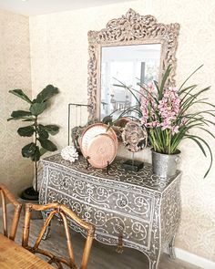 a table with a mirror and some plants on it in front of a chair next to a potted plant