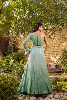 Radiate elegance in this exquisite green ombre lehenga set by Suruchi Parakh! Crafted from georgette crepe, this embellished ensemble exudes glamour with its intricate sequin work and delicate floral embroidery. The matching one-shoulder crop top features stunning feather detailing, perfectly complementing the organza ruffled dupatta. This masterpiece is a must-have addition to your ethnic wardrobe and sure to turn heads at any special occasion. Pista Green Floor-length Dress With Sequins, Elegant Pista Green Lehenga With Sequins, Elegant Pista Green Sequined Lehenga, Glamorous Green Lehenga, Pista Green Sequined Georgette Lehenga, Glamorous Green Festive Gown, Glamorous Festive Green Gown, Glamorous Green Lehenga For Reception, Glamorous Green Lehenga For Wedding