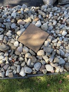 there is a square stone in the middle of some rocks on the ground and grass