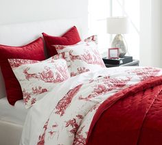 a bed with red and white comforters in a bedroom next to a lamp on a table