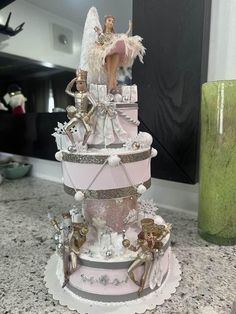 a pink and silver wedding cake with angel figurines on top, sitting on a counter