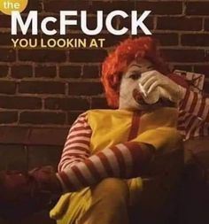 a clown sitting on top of a couch next to a brick wall with the words mcfuck you lookin at