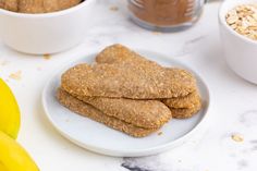 three cookies on a plate next to bananas and oatmeal in small bowls