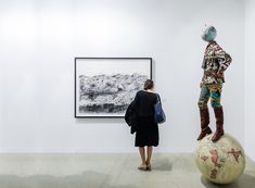 a woman looking at an art work on display in a room with white walls and flooring