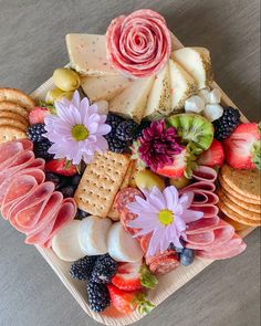 a platter filled with cheese, crackers, fruit and flowers