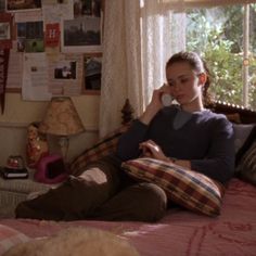 a woman is sitting on her bed talking on the phone