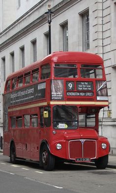 a red double decker bus parked on the side of the road in front of a building