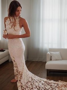 a woman standing in a living room wearing a white dress and holding a gold cup