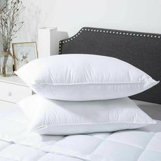 two pillows are stacked on top of each other in front of a bed with white sheets