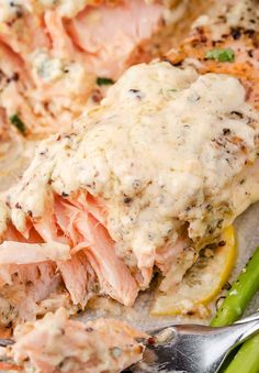 a plate with salmon and asparagus covered in cream sauce next to a fork