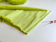 a pair of scissors and green cloth on a white table with needles in the foreground