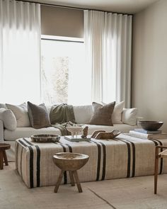 a living room filled with lots of furniture next to a large window covered in white curtains