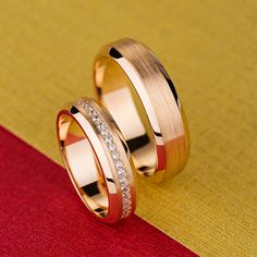 two gold wedding rings with diamonds on them sitting on a red and yellow carpeted surface