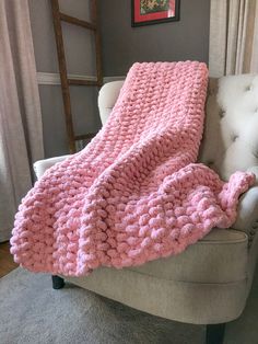 a pink knitted blanket sitting on top of a chair next to a white chair