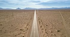 an aerial view of a long stretch of road in the desert with mountains in the background