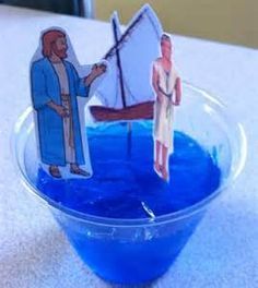 a bowl with blue liquid and paper cutouts in the shape of people on boats