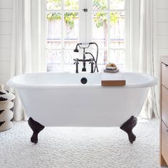 a white bath tub sitting under a window next to a wooden cabinet in a bathroom