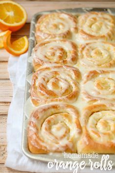 orange rolls on a baking sheet next to sliced oranges