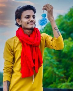 a man wearing a yellow shirt and red scarf holding up a blue item in his hand