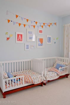 two white cribs in a blue room with bunting flags on the wall