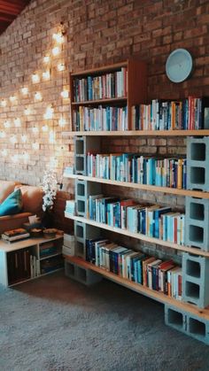 a book shelf filled with lots of books on top of a carpeted floor next to a brick wall