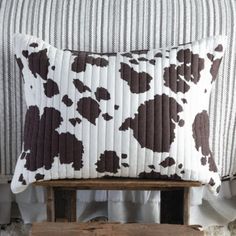 a brown and white cow print pillow sitting on top of a wooden bench next to a bed