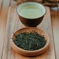 a wooden bowl filled with green tea next to a cup full of liquid on top of a table