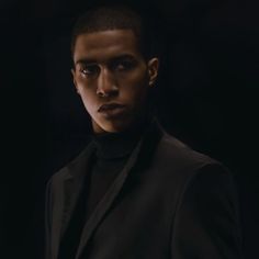 a young man in a black suit and turtle neck sweater looking at the camera with an intense look on his face