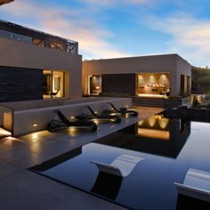 an outdoor pool with lounge chairs and grill on the patio at dusk, next to a modern home