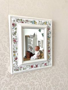 a small child's reflection in a white frame on a wall with floral designs