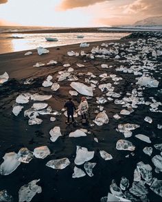 two people are walking on the beach near icebergs that have been washed ashore