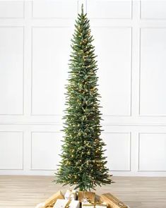 a christmas tree with presents under it on a wooden floor in front of a white wall