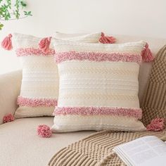 two pillows with tassels sit on a couch next to a book and potted plant